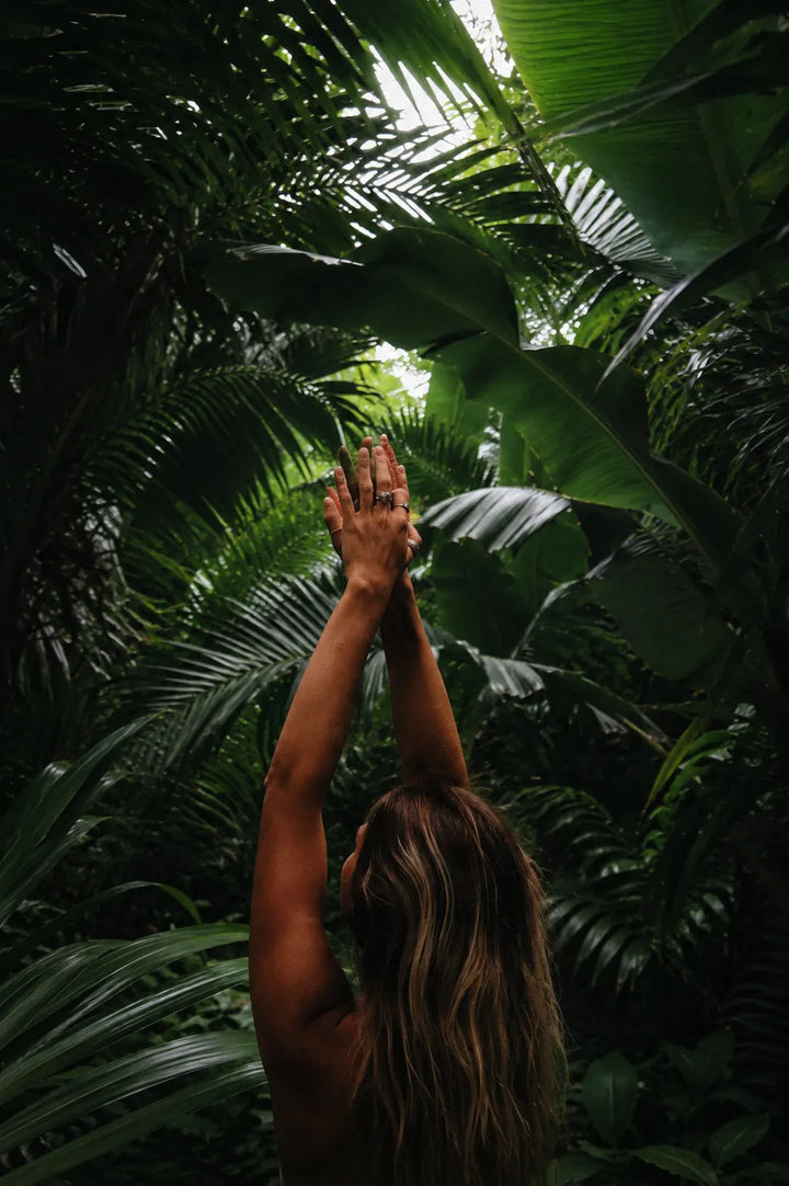 Femme de dos, les bras levés vers la canopée d'une forêt tropicale